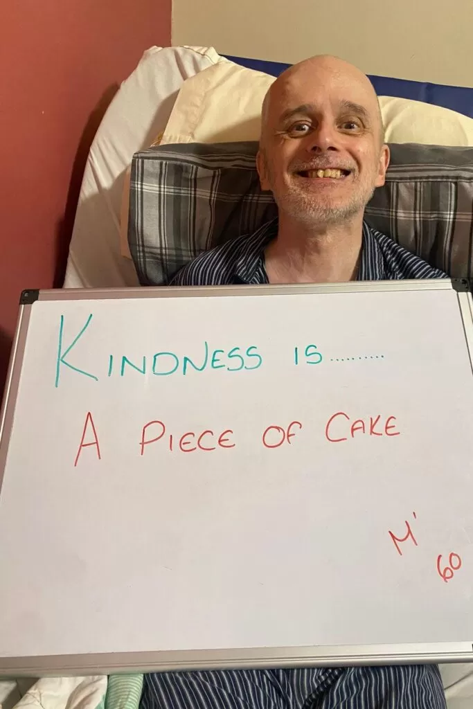 a man holding up a board that says "Kindness is a piece of cake"